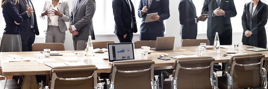 L'immagine raffigura un tavolo di lavoro, intorno al quale ci sono una serie di persone che discutono tra loro in piedi